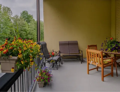 Covered balcony with chairs, a wooden table and flower-filled planters.