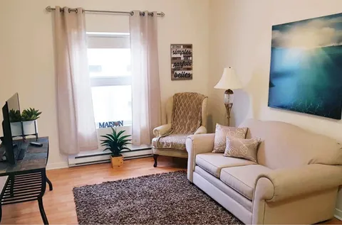 Suite sitting area with a beige sofa, armchair, television and landscape artwork.