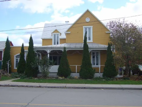 Front of the yellow residence behind trees and shrubs.