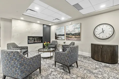 Patterned armchairs beside a fireplace, landscape paintings and a wall clock
