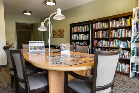 Library shelves and a round table with chairs and a jigsaw puzzle.