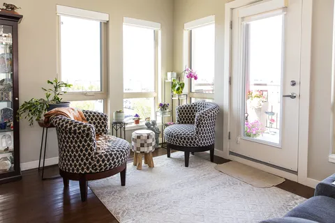 Sitting area with two chairs beside tall windows and a glass door.