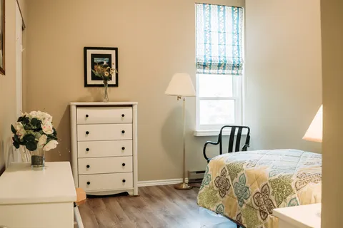 Bedroom with a patterned quilt, white drawers and a window