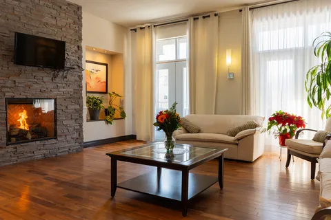 Sitting room with a sofa, glass coffee table, stone fireplace and tall curtained windows
