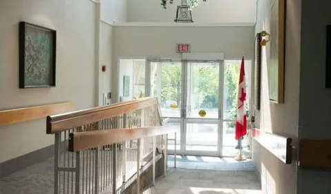 Glass entrance doors beside a ramp, metal railing and Canadian flag