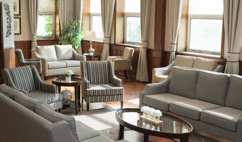 Sofas and striped armchairs beside tall windows and wooden panelling