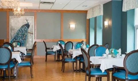 Dining tables with blue chairs, white tablecloths and a peacock painting