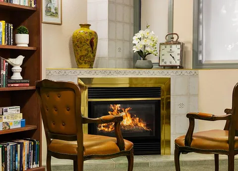 Leather chairs and bookshelves beside a tiled fireplace.