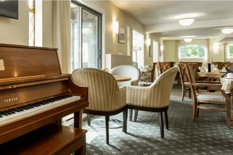 Dining area with upholstered chairs and a piano by the windows.