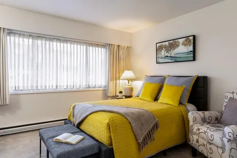 Bedroom with a bed, bedside table and a large curtained window.