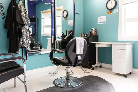 Salon with a black styling chair, wall mirrors and turquoise walls