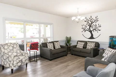 Sitting area with grey sofas, patterned armchairs, a tree mural and an aquarium