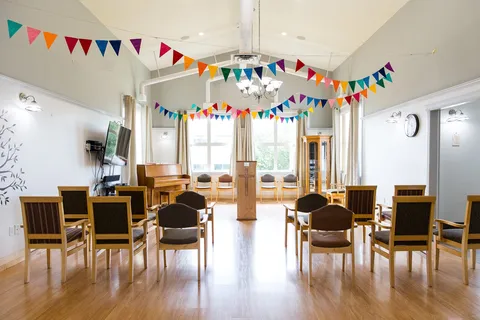 Room with rows of chairs, a podium, a piano and colourful bunting