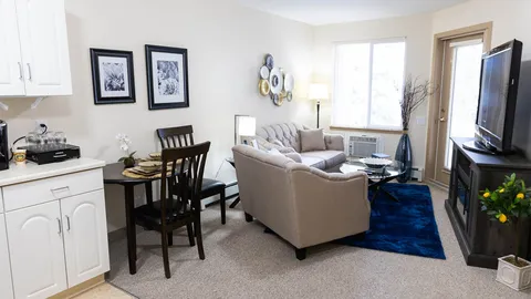 Sitting area with grey sofas, a glass coffee table, blue rug and a kitchenette