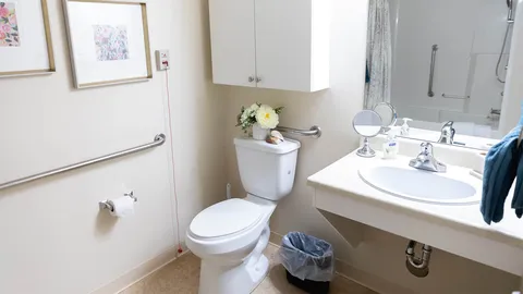 Bathroom with a sink, toilet, wall mirror, grab bars and floral pictures