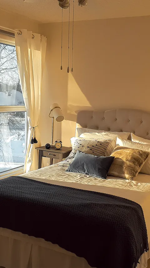 Bedroom with a padded headboard, cushions and a window.