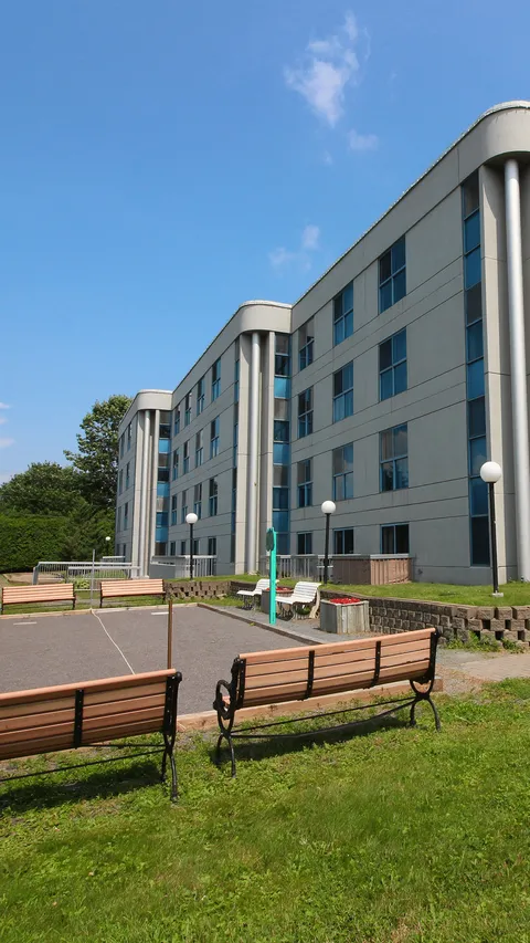 Residence facade beside lawns, benches and an outdoor path.