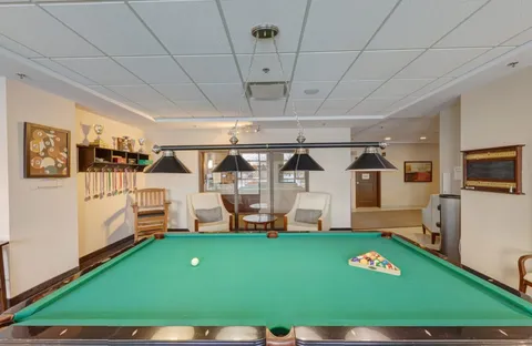 Green billiard table beneath hanging lights, with armchairs and cue racks