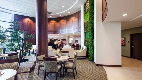 Seating area with armchairs, round tables, a piano and a green plant wall