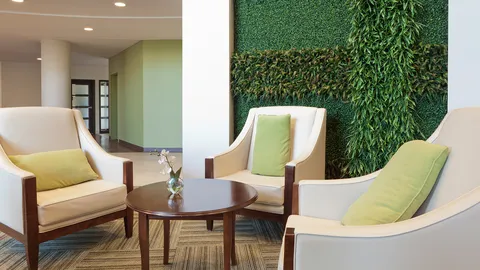 Cream armchairs with green cushions beside a living plant wall