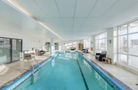 Indoor swimming pool with handrails, chairs and tall windows