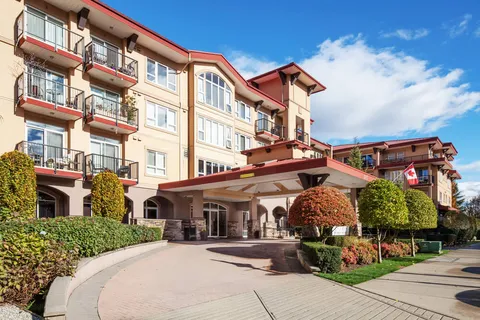 Multi-storey residence with balconies, a covered entrance and trimmed shrubs beside a curved driveway