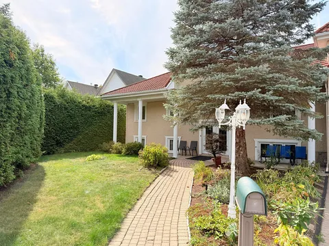Brick garden path beside a lawn, hedges, flower beds and a beige brick building