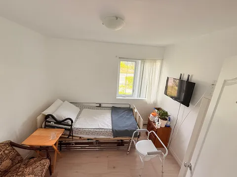 Bedroom with an adjustable bed, floral armchair, wooden table, television and window