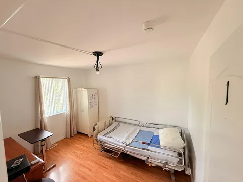 Bedroom with an adjustable bed, wardrobe, small table, wood flooring and a curtained window