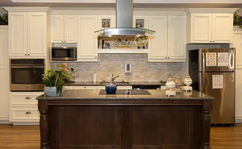 Kitchen with white cabinets, a dark island, oven, microwave and refrigerator