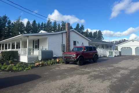 White single-storey building with a long covered porch, lawn and parked cars
