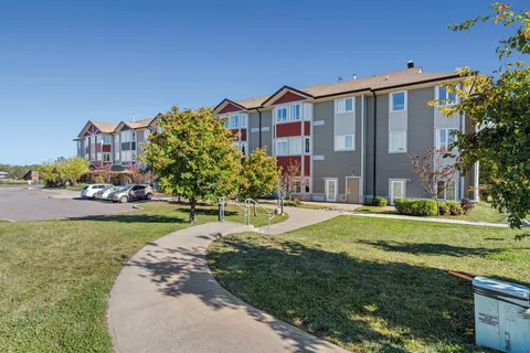Three-storey building beside a lawn, trees and parking area