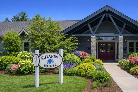 Single-storey building entrance with a covered porch, garden beds and a paved path