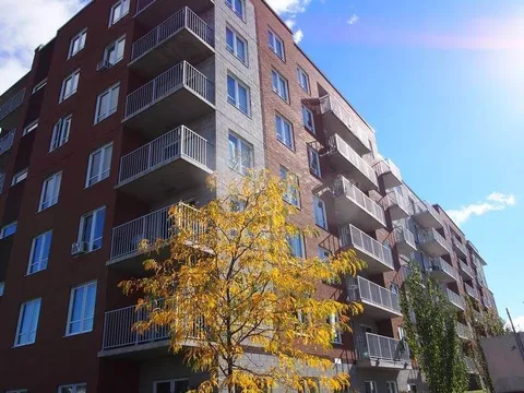 Brick residence facade with balconies and a tree in front.