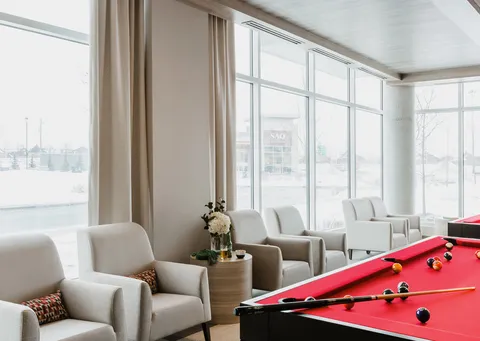 Red billiard table beside cream armchairs and large windows