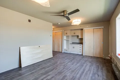 Empty room with a ceiling fan, kitchenette and grey flooring