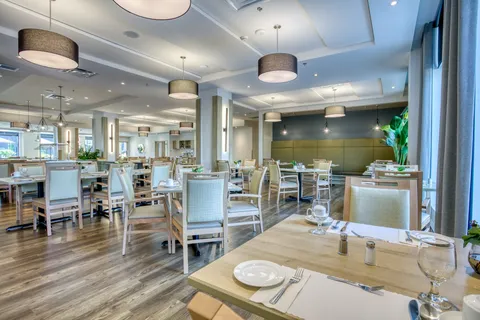 Dining room with set tables, upholstered chairs and pendant lights.