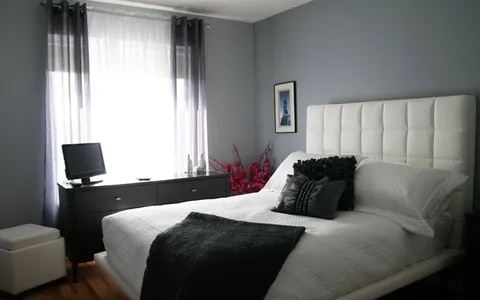 Bedroom with a white bed, dark blanket, dresser, television and a blue framed print