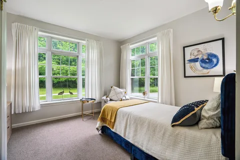 Bedroom with a bed, armchair and large windows overlooking trees.