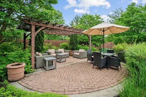 Brick garden patio with wicker chairs, tables, a pergola and an umbrella.