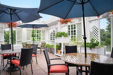 Patio tables and chairs beneath umbrellas beside white lattice screens.