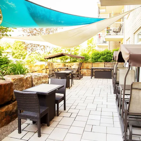 Paved patio with wicker chairs, tables, shade sails and planted stone borders.