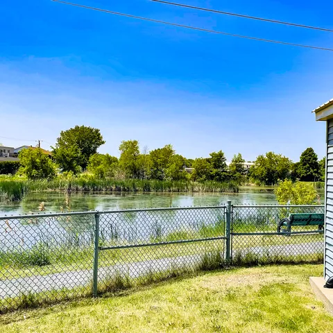 Lawn and a green bench beside a chain-link fence overlooking the river.