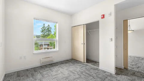 Empty carpeted bedroom with an open closet and a large window