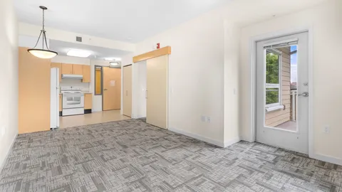 Empty carpeted room with a kitchenette, pendant light and balcony door