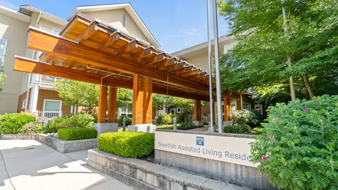 Covered timber entrance beside shrubs and a residence sign