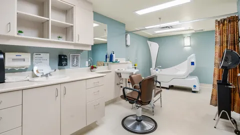 Room with a styling chair, sink, cupboards and accessible bathing equipment