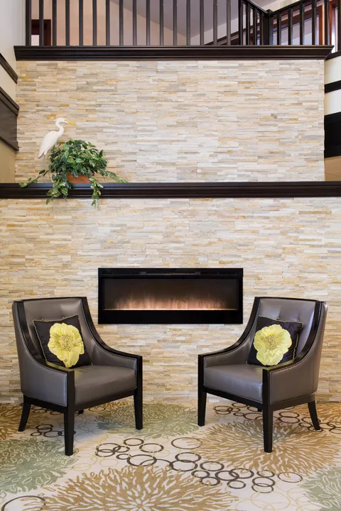 Lobby chairs beside a stone fireplace beneath an upper railing.