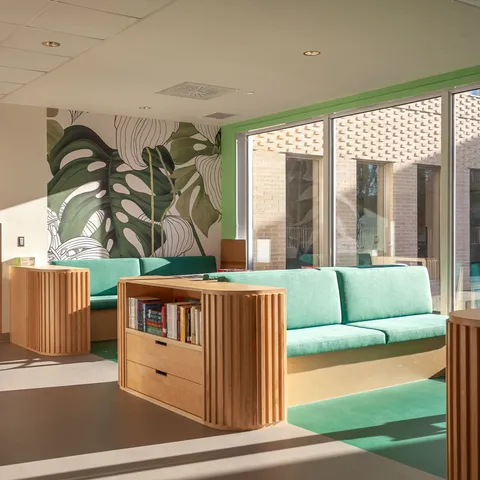 Green upholstered seating with bookshelves beside large windows