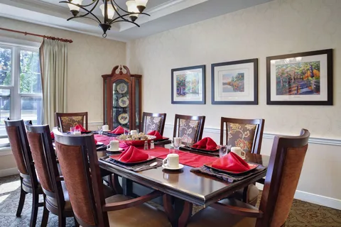 Private dining table with red napkins, wooden chairs and framed landscapes.